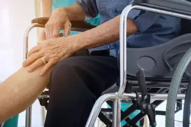 Elderly patient in wheelchair holding painful knee, seeking arthritis treatment from Dr. Sumit Kumar Jha in Siliguri